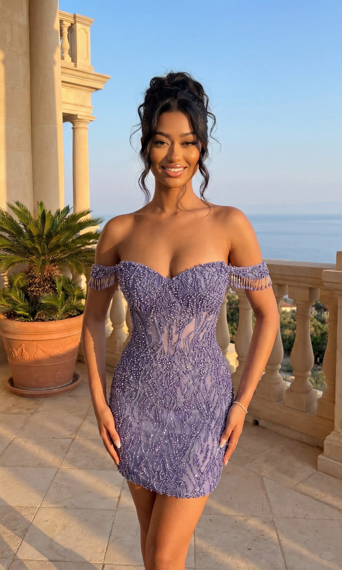 Smiling woman stands on a balcony with a sea view, wearing the purple Beaded Glitter Hoco Dress: PromGirl Exclusive 250133—a short, off-the-shoulder homecoming dress adorned with beads and glitter.